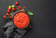 Tomato sauce in a frying pan on a wooden board on a black background. Marinara sauce with basil. Top view, copy space.