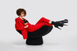 Dancer woman in red pantsui and pole dance boots sits in a soft chair