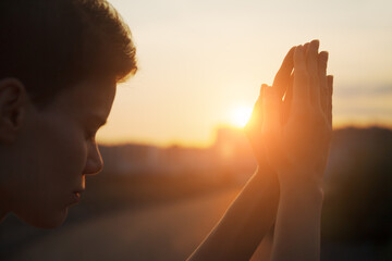 Hands of young christian woman praying at sunrise light, religion and spirituality concept