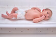 A newborn baby in diapers on a white changing table with a ruler for measuring full height.