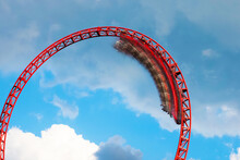 Roller Coaster Ride Filled With Thrill Seekers Doing Loop, Cloudy Sky Background. Roller Coaster. Wagon In Motion