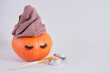 Brush, Aluminum Jar With Cosmetic Clay Face Mask And Orange Pumpkin With Towel And False Eyelashes On Gray Background