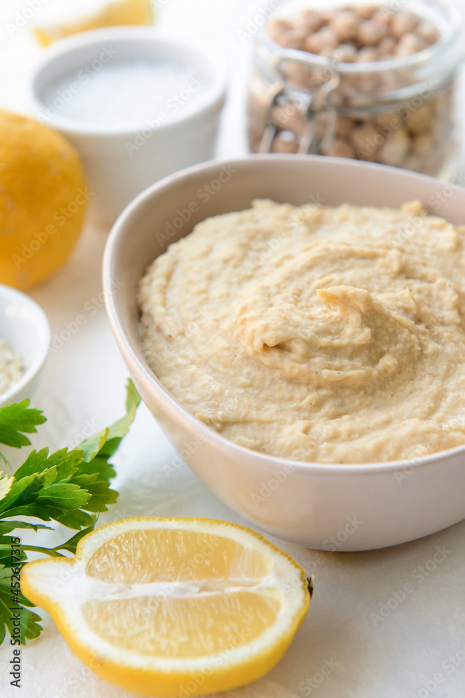 Bowl with tasty hummus and lemon on light background