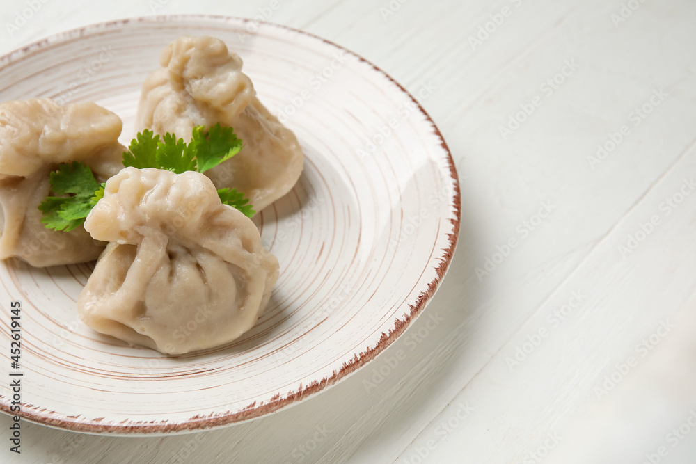 Plate with tasty dumplings on light wooden background, closeup