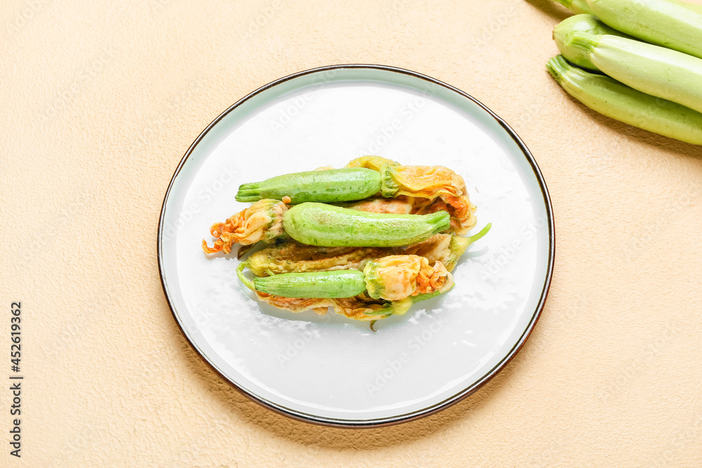 Plate with fried zucchini flowers on color background