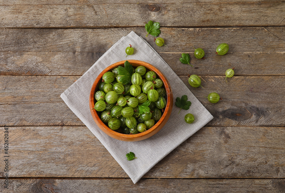 Bowl with fresh ripe gooseberry on wooden background