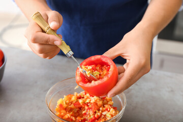 Woman preparing stuffed tomatoes at table in kitchen, closeup