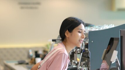 Wall Mural - 4K Young beautiful Asian woman coffee shop employee barista working at cafe. Smiling female cashier taking order coffee and bakery from customer. Small business owner and part time job working concept