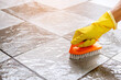 © ETAP - Hands wearing yellow rubber gloves are using a plastic floor scrubber to scrub the tile floor with a floor cleaner.
