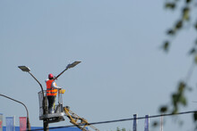 Street Light. A Worker In Special Clothes And A Helmet Repairs A Street Lamp On A City Street.