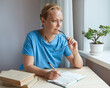 © evafesenuk - adult woman is sitting at a table, uses a diary, she is thinking, taking off her glasses