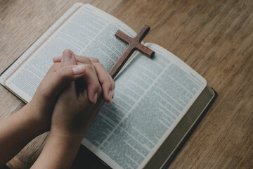 Wall Mural - Woman with wooden cross in hands praying for blessing from god on old bible book. Spirtuality and religion, Religious concepts