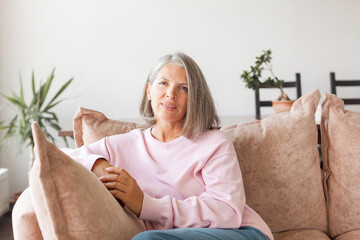 Portrait happy healthy middle aged woman sitting on comfortable couch at home