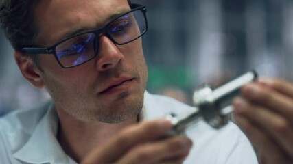 Leinwandbilder - Close Up Portrait of Young Handsome Engineer in Glasses Working on Manufacturing Metal Parts in Office at Car Assembly Plant. Industrial Product Designer Examining Prototype Parts Before Production.