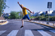 © Manuel - Hispanic mature adult man with hat, mustard-colored t-shirt and short jeans making fun jumps over a crosswalk in the middle of the city.