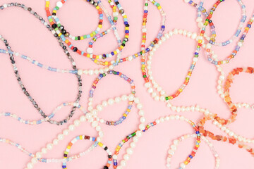 Necklaces and bracelets made from multicolored beads and pearls on a pink pastel background.