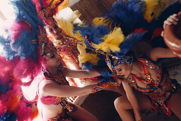 Wall Mural - Woman in brazilian samba carnival costume with colorful feathers plumage relax in old entrance with big window.