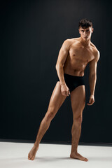 Wall Mural - sporty man with a muscular body in black shorts posing dark background