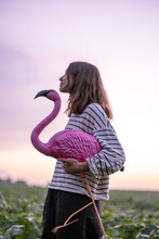 Carefree Woman With Pink Flamingo On Potato Field In The Evening, Enjoying Sunset And Purple Sky