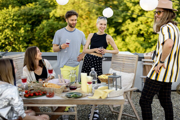 Young group of stylish people having a festive dinner on the roof terrace. Friends hanging out and having great summertime together outdoors