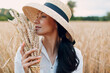 Young Woman in straw hat holding sheaf of wheat ears at agricultural field.