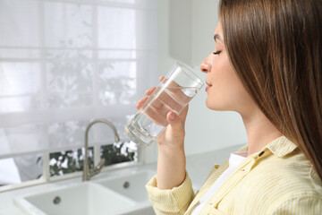 Wall Mural - Woman drinking tap water from glass in kitchen