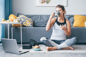 woman sitting and drinking coffee after workout session at home.