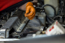 A Man Wearing An Orange Glove Fixing And Doing Maintenace On A Car Engine In An Auto Repair Shop