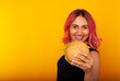 © Marina Chernivetskay - a woman with bright pink hair shows a delicious burger with a smile on her face charming. Advertising fast food, I love junk food. vs vegans. Vegan Burger Without Meat. space for text