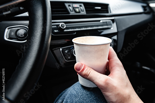 Hand holding paper coffee cup behind the wheel..Takeaway drink.