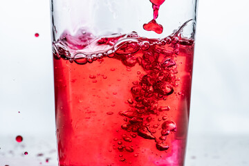 Red liquid being poured into a glass. White background..