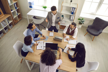 Wall Mural - Team of businesspeople having a discussion in a meeting. Group of young and mature business teammates sitting around table in office interior and listening to manager. View from above, high angle shot