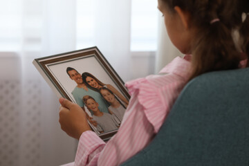 Poster - Little girl holding framed family photo indoors, closeup