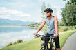 © Soloviova Liudmyla - Portrait of a sincerely smiling man dressed in cycling clothes, helmet and sunglasses riding a bicycle on the asphalt out-of-town bicycle path along a mount lake. Active sporty people concept image.