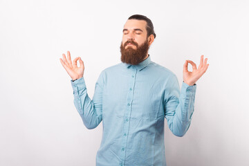 Calm bearded man is making the zen gesture in a studio over white background.