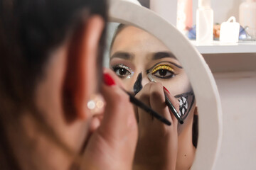 Beautiful girl lining her eyes with Halloween makeup in her bedroom.