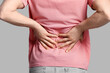 © Pixel-Shot - Young man suffering from back pain on grey background