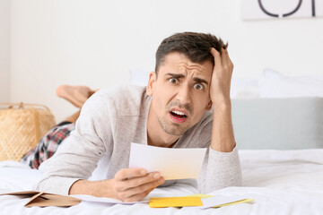 Wall Mural - Shocked young man reading letter in bedroom