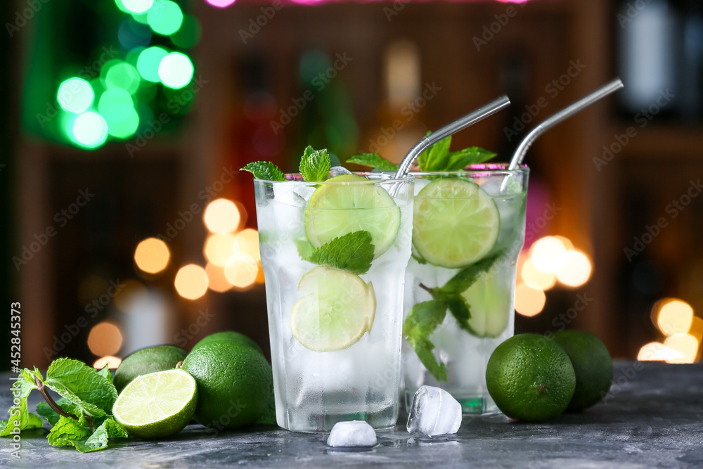 Glasses of cold mojito on table against blurred lights
