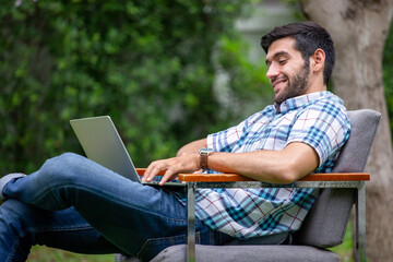 young handsome man freelancer sitting on chair in front yard  using laptop computer working at home .