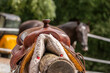 Close-up of a western saddle with a black horse in the background