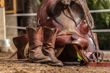  Ranch life scenery: muddy western boots in front of a western saddle. Cowboy boots. Muddy working boots