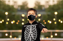Halloween, Holiday And Pandemic Concept - Boy In Black Protective Mask And Costume Of Skeleton Pointing Finger To Camera Over Garland Lights At Roof Top Party Background