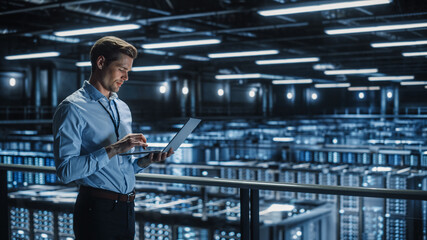 Wall Mural - Portrait of IT Specialist Uses Laptop in Data Center. Server Farm Cloud Computing Facility with Male Maintenance Administrator Working. Cyber Security and Network Protection.