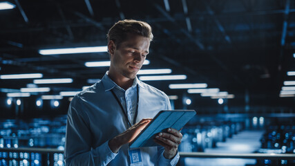 Wall Mural - Portrait of Handsome Smiling IT Specialist Using Tablet Computer in Data Center, Looking at Camera. Succesful Male e-Business Engineer Working in Big Server Farm Cloud Computing Facility.