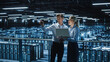 © Gorodenkoff - Data Center Female e-Business Enrepreneur and Male IT Specialist talk, Use Laptop. Two Information Technology Engineers work on Bridge Big Cloud Computing Server Farm.