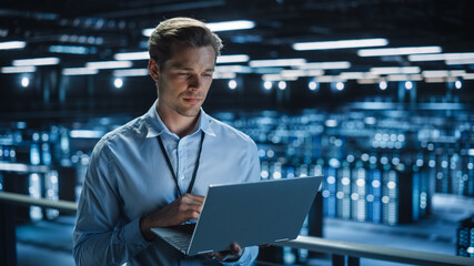Leinwandbilder - Handsome Smiling IT Specialist Using Laptop Computer in Data Center. Succesful Businessman and e-Business Entrepreneur Overlooking Server Farm Cloud Computing Facility.