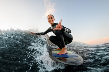 Wall Mural - smiling woman sits on wakesurf board and rides the wave and touches the waves with one hand