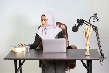 Wall Mural - muslim business woman looking down at the books during working on laptop computer in her desk