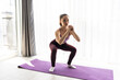 © dianagrytsku - Attractive young woman in sportswear doing sit-ups in living room, training legs, trying to form perfect butt shape, squatting at home.